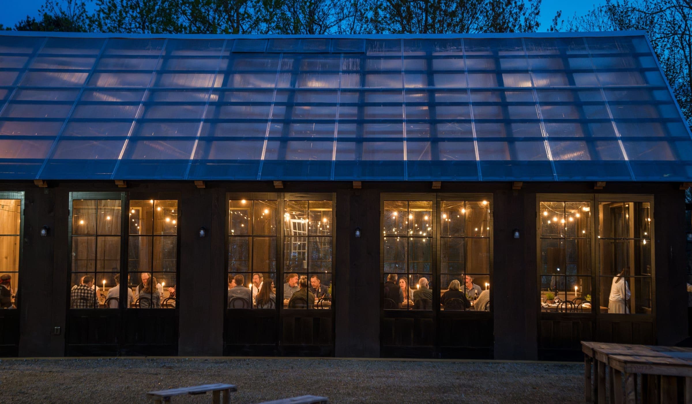 The Glass House at blue hour, a long table lit inside.